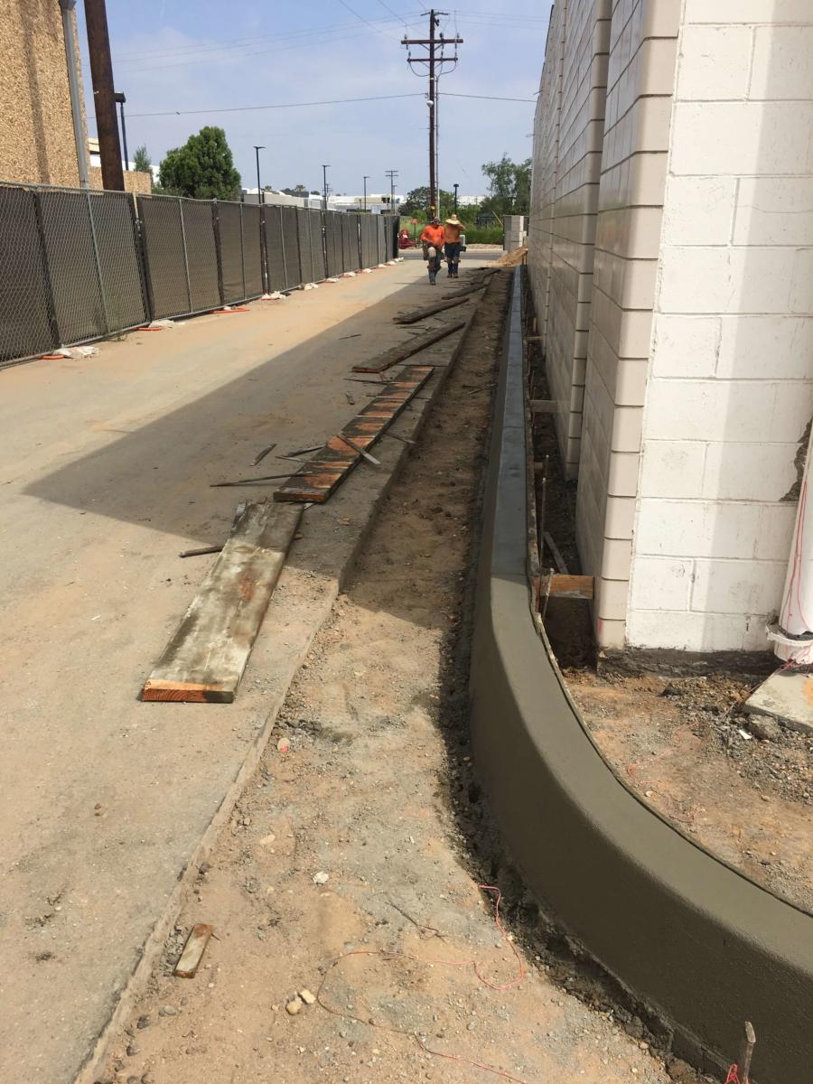 Fresh concrete curb poured along a building wall, crew working a commercial sitework job